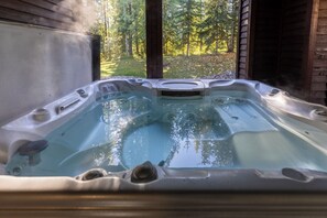 A hot tub with a view of a forest through an open wooden structure.