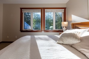 A bedroom with a large bed, a nightstand, a lamp, and a window with a view of trees.