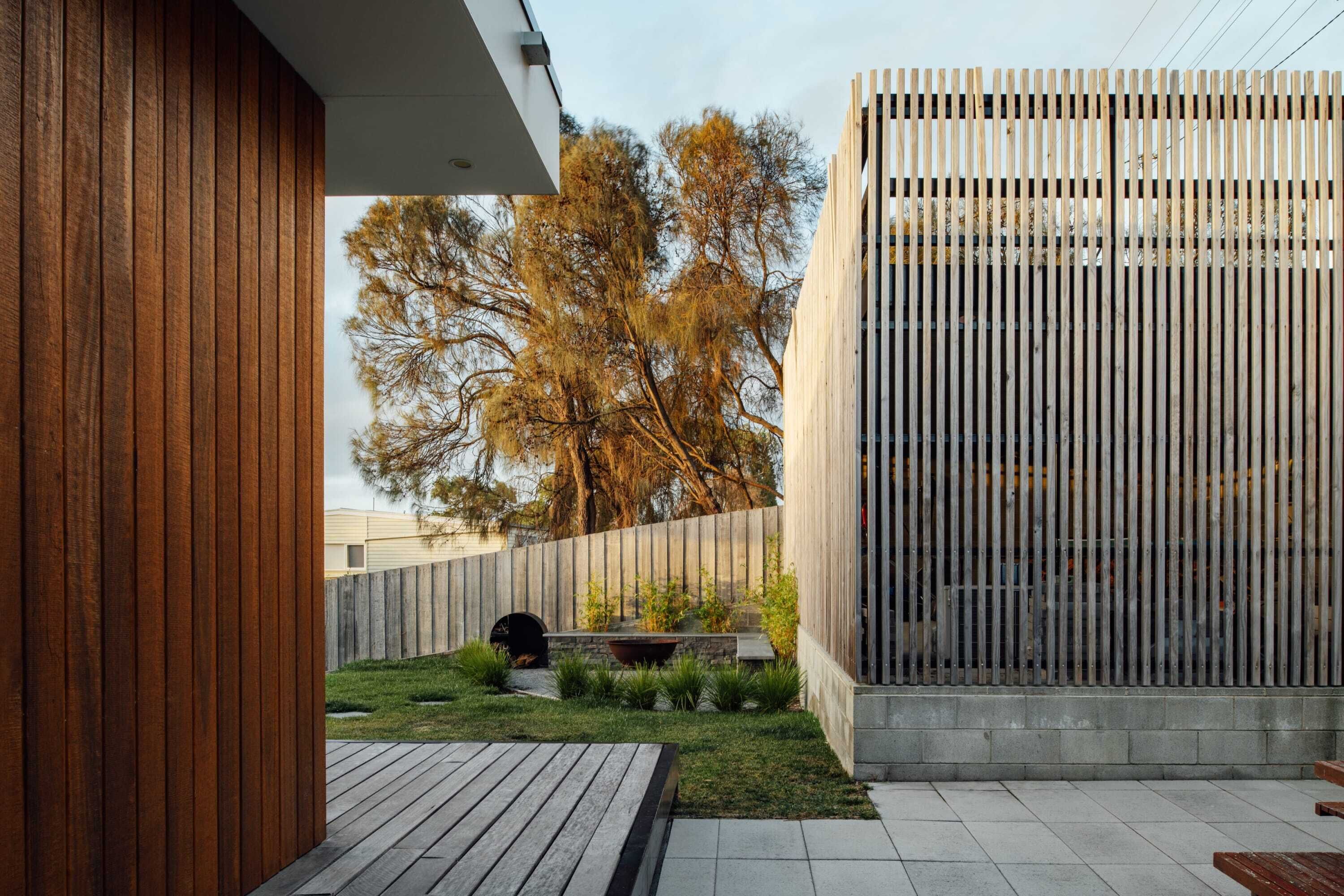 Ein moderner Außenbereich mit einer Holzdielen-Terrasse, einer Sitzgruppe aus Beton und einem Metallzaun.