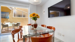 Un comedor moderno con una mesa de vidrio, sillas naranjas y un jarrón de girasoles.