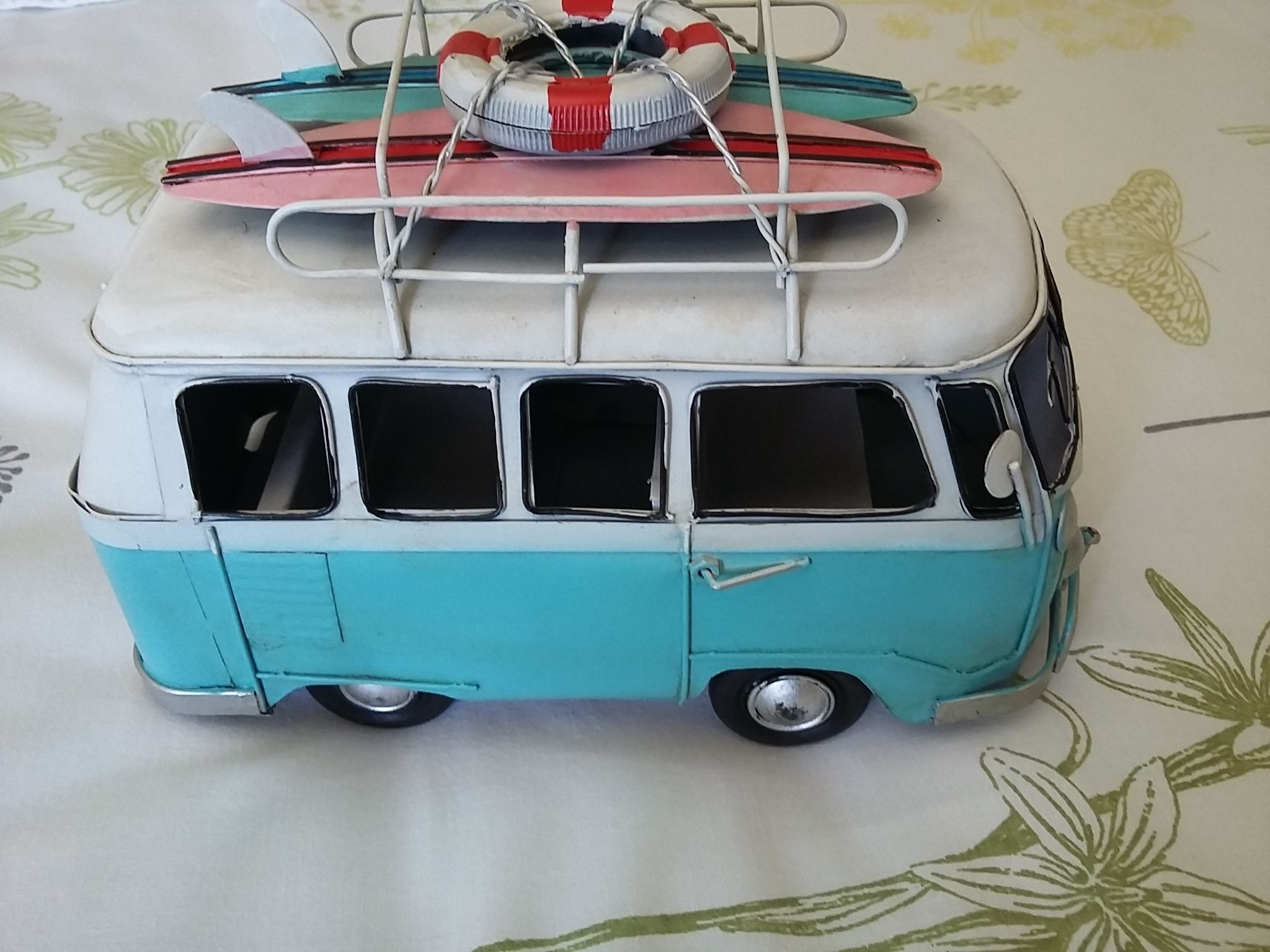 A vintage teal and white van with a roof rack, a life preserver, and a surfboard.