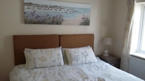 A bedroom with a bed, a nightstand, a lamp, and a painting of a coastal scene. - Harrington Flats (Newquay)