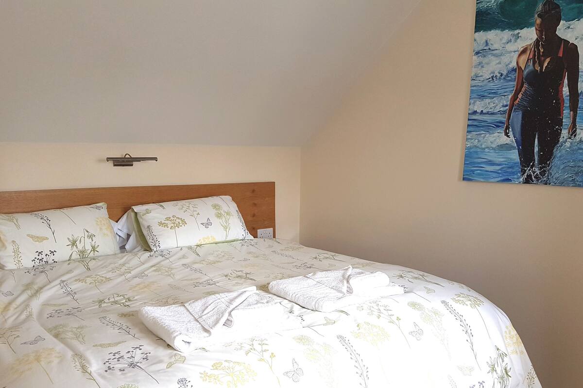 A neatly made bed with floral bedding, a wooden headboard, and a wall-mounted light fixture.