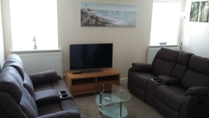 A living room with two sofas, a glass coffee table, a TV on a wooden stand, and a painting on the wall. - Harrington Flats (Newquay)