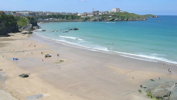 A beach with clear turquoise waters, a sandy shore, and buildings in the background. - Harrington Flats (Newquay)