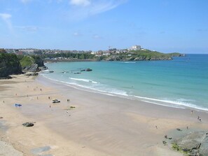 A beach with clear turquoise waters, a sandy shore, and buildings in the background.