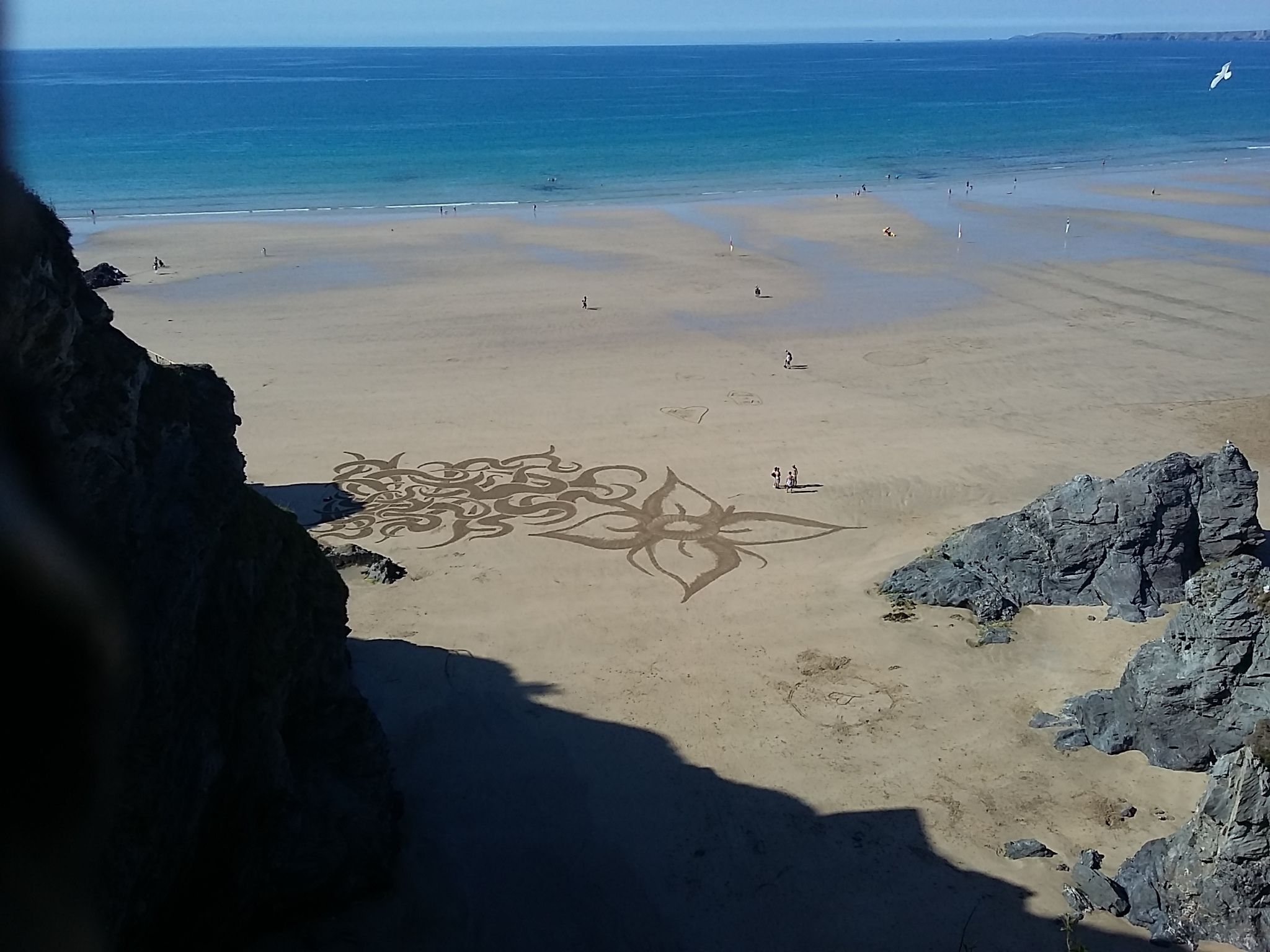 Une plage avec une grande formation rocheuse sur la gauche et une vue dégagée sur l’océan.