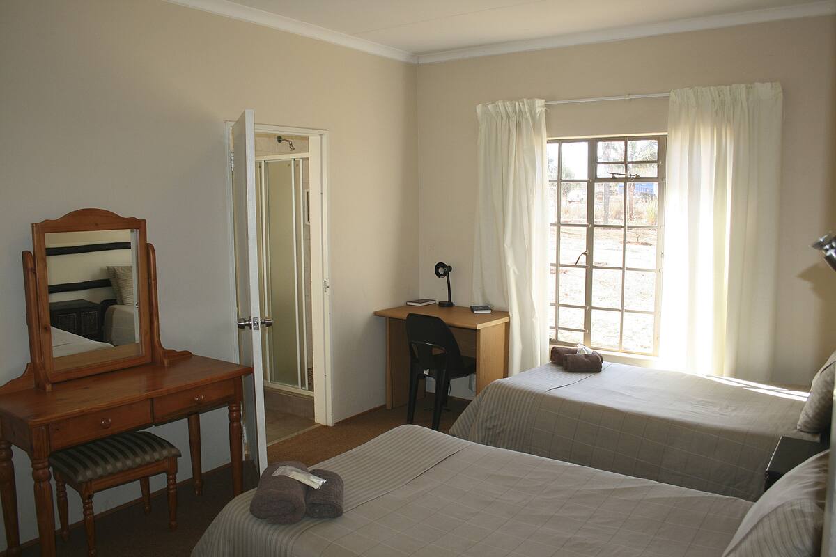 Une chambre d’hôtel avec deux lits, un bureau, une chaise, un miroir et une fenêtre avec des rideaux.