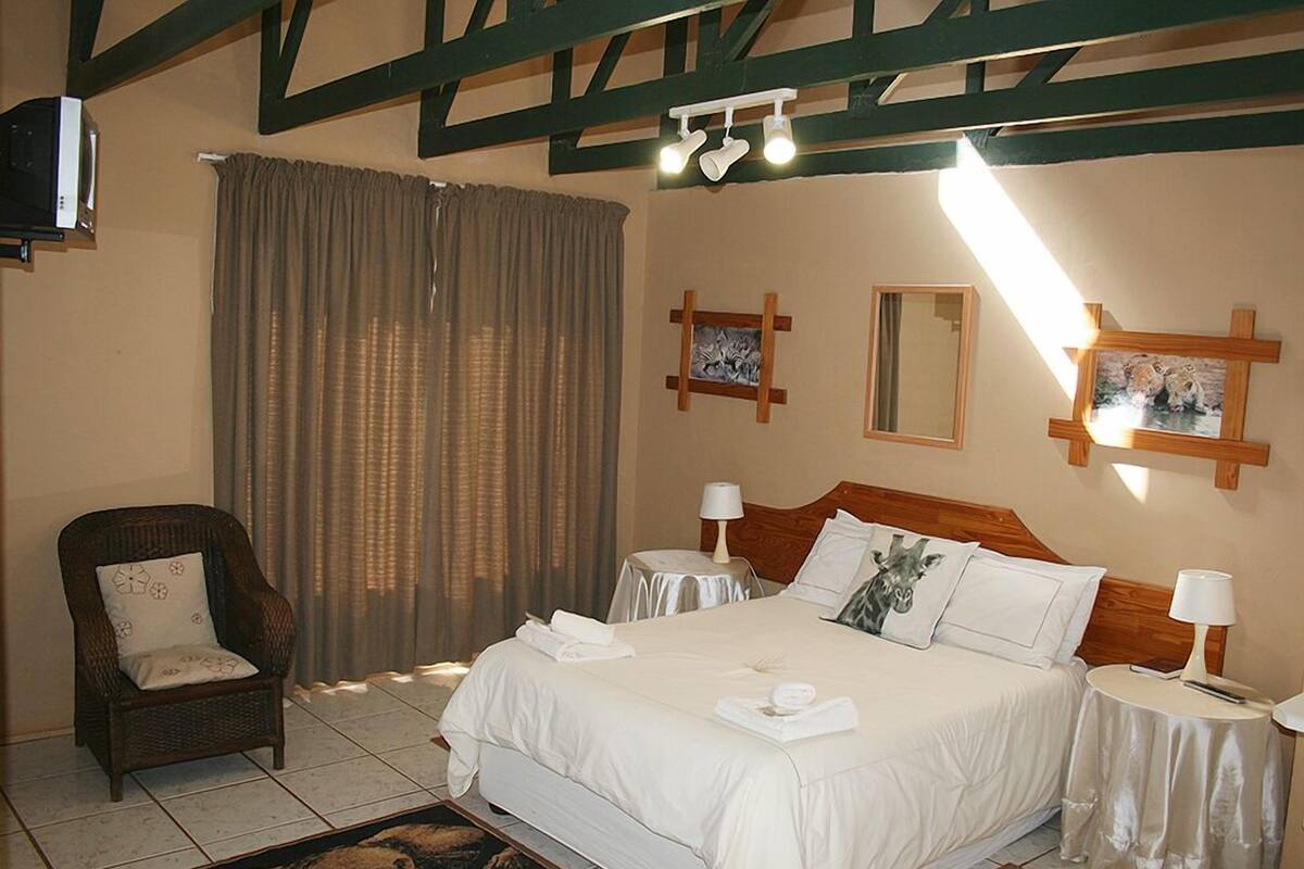 Une chambre d’hôtel avec un grand lit, une chaise, un téléviseur et un ventilateur de plafond.