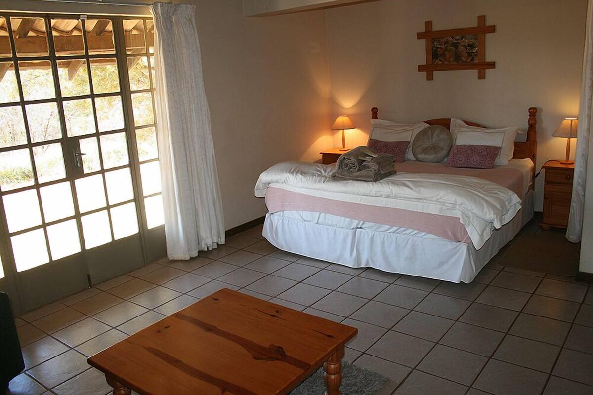 Une chambre à coucher avec un lit, des lampes de chevet, une table en bois et une fenêtre avec des rideaux.