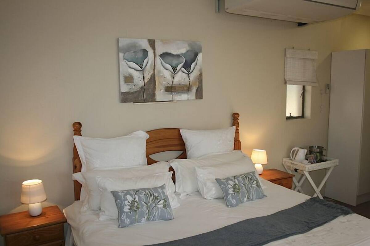 Un lit bien fait, avec du linge de lit blanc et des coussins à motifs floraux, une tête de lit en bois et deux lampes de chevet.