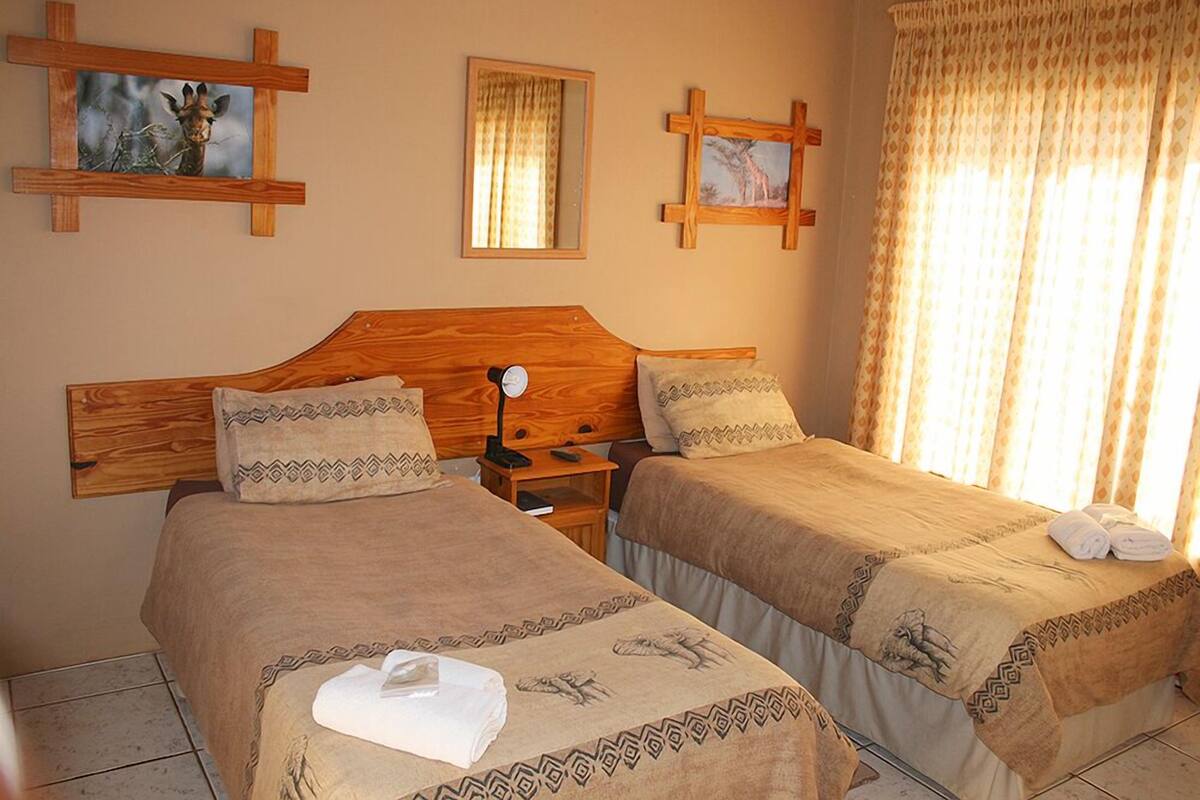 Une chambre d’hôtel avec deux lits, des têtes de lit en bois et une grande fenêtre avec des rideaux.