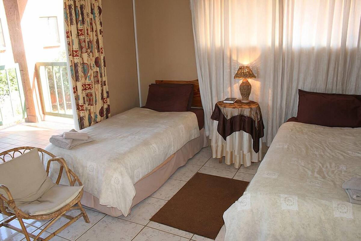 Une chambre d’hôtel avec deux lits, une petite table avec une lampe, un fauteuil en osier et une vue sur l’extérieur.