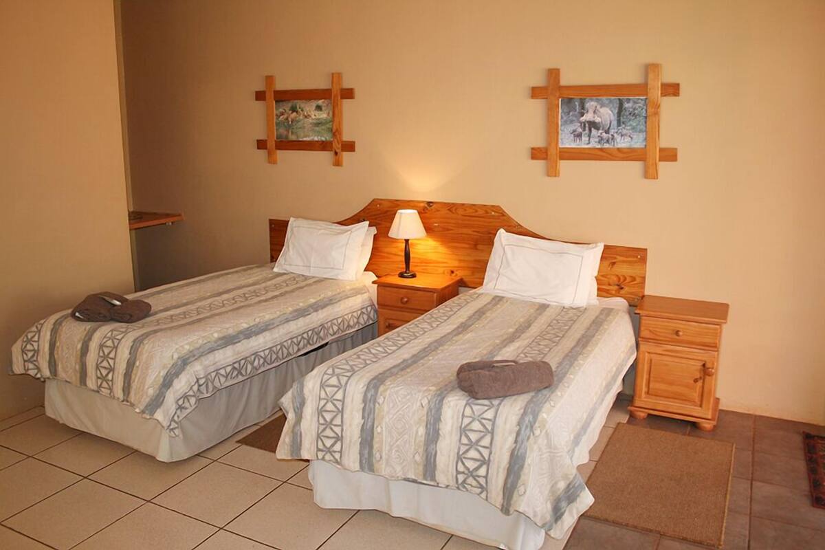 Une chambre avec deux lits, chacun doté d’une tête de lit en bois, d’une table de chevet et d’une lampe. Deux tableaux ornent les murs.