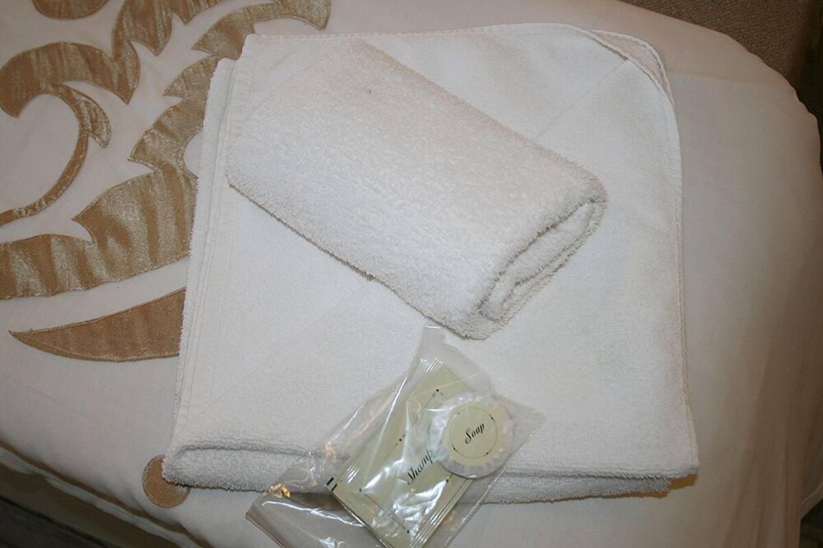 Une serviette blanche soigneusement pliée et un petit sac en plastique contenant un savon sont posés sur un lit doté d’une tête de lit décorative.