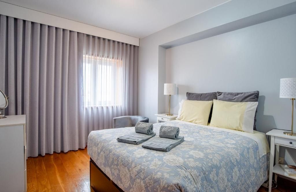 Une chambre d’hôtel avec un lit, deux tables de chevet, une chaise, un bureau et une fenêtre avec des rideaux.