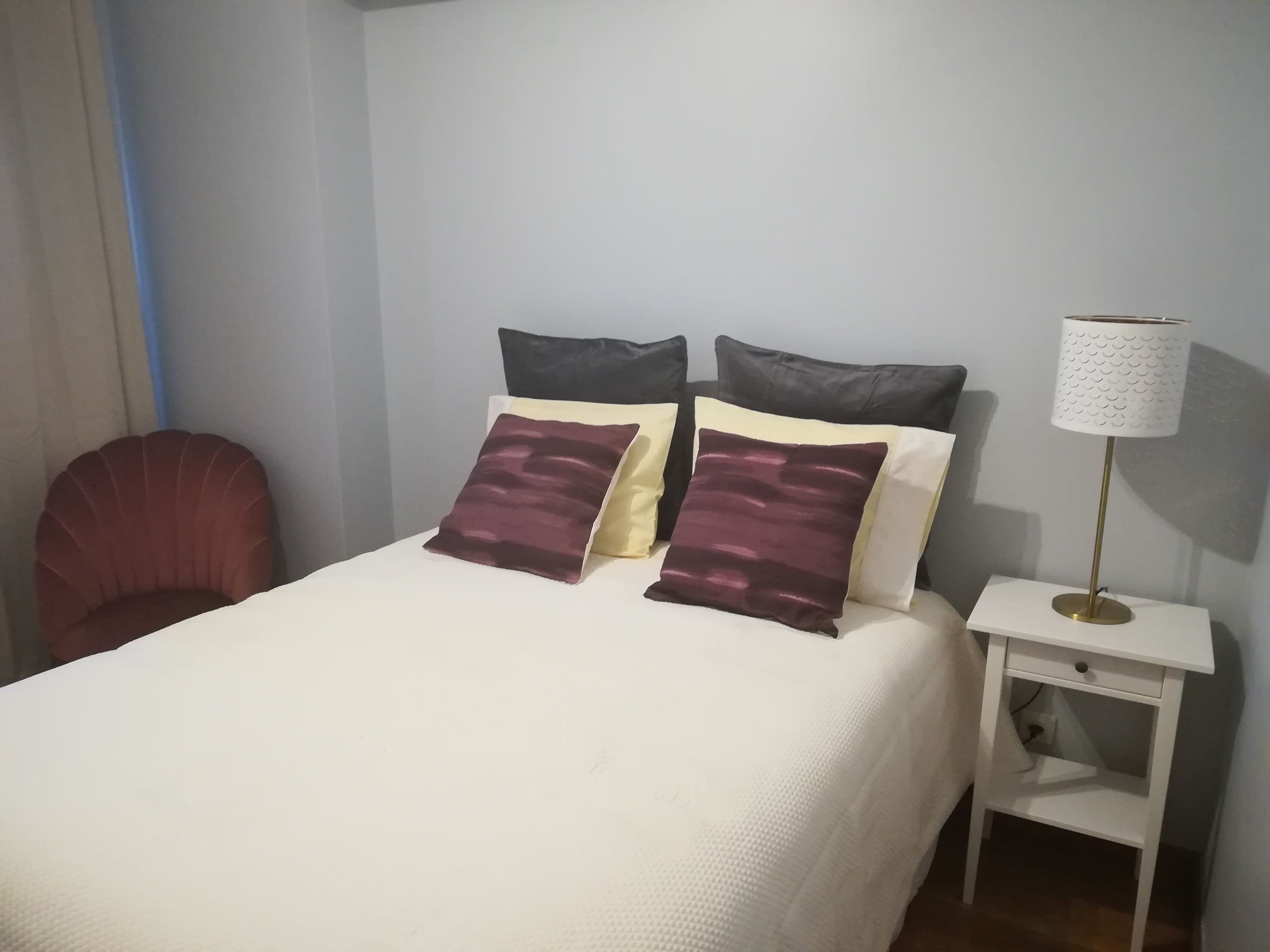 A neatly made bed with two pillows, a bedside table with a lamp, and a chair.