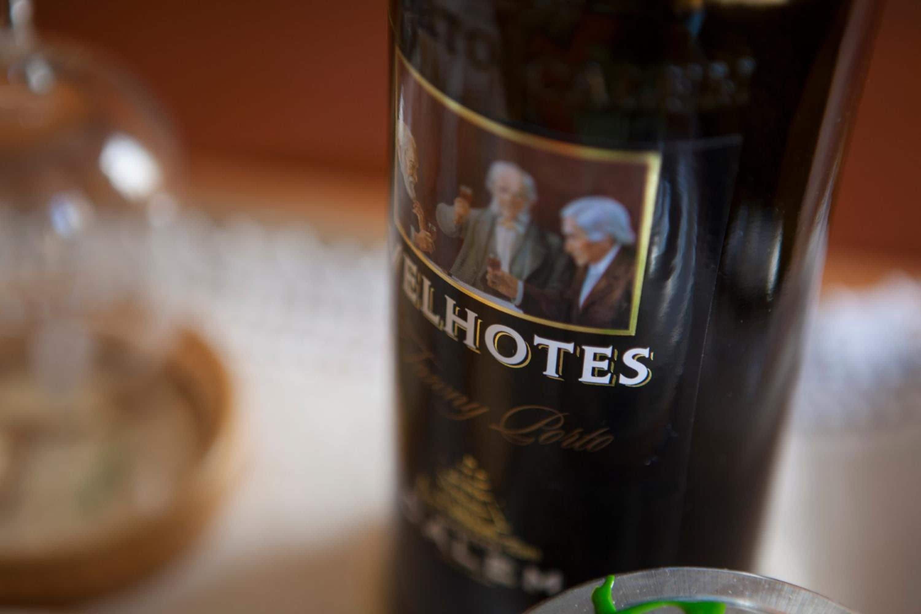 Een fles wijn met een etiket waarop de naam 'HOTES' staat en een portret van twee personen.