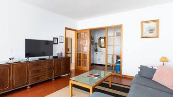 A living room with a sofa, a coffee table, a TV, a wooden cabinet, and a sliding door leading to a kitchen.