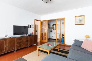 A living room with a sofa, a coffee table, a TV, a wooden cabinet, and a sliding door leading to a kitchen. - Avenida Apartment by MP (Vila Nova de Gaia)