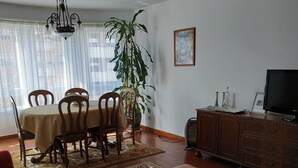 Una sala de estar con una mesa de comedor, sillas, un sofá, una mesa de centro, un televisor, un mueble y una planta grande.
