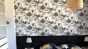 Una camera da letto con un letto, un comodino, una lampada, un lampadario intrecciato e una parete decorata con un motivo a palma.