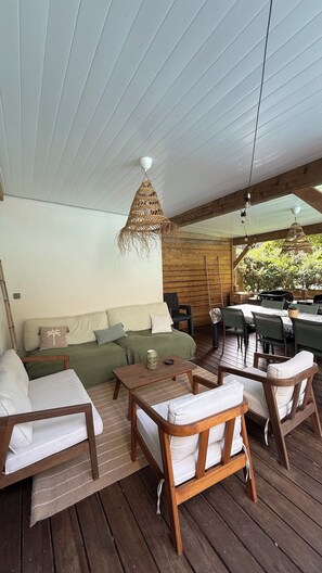A covered outdoor seating area with wooden furniture, a woven hanging light fixture, and a view of greenery outside. - ONDRES Villa near beach with pool and spa  (Ondres)