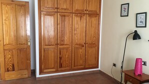 Ein Zimmer mit großem Holzschrank, Nachttisch mit Lampe und einem Bett.