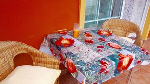 Ein kleiner Tisch im Freien mit einer blumigen Tischdecke, Korbstühle und ein Glas Orangensaft.