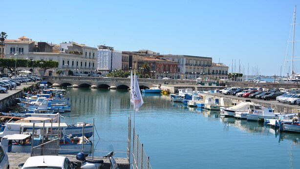 Marina com barcos atracados, uma ponte e edifícios ao fundo.