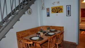 Uma sala de jantar com mesa de madeira posta para quatro pessoas, escada e decorações nas paredes, incluindo um relógio e quadros emoldurados.
