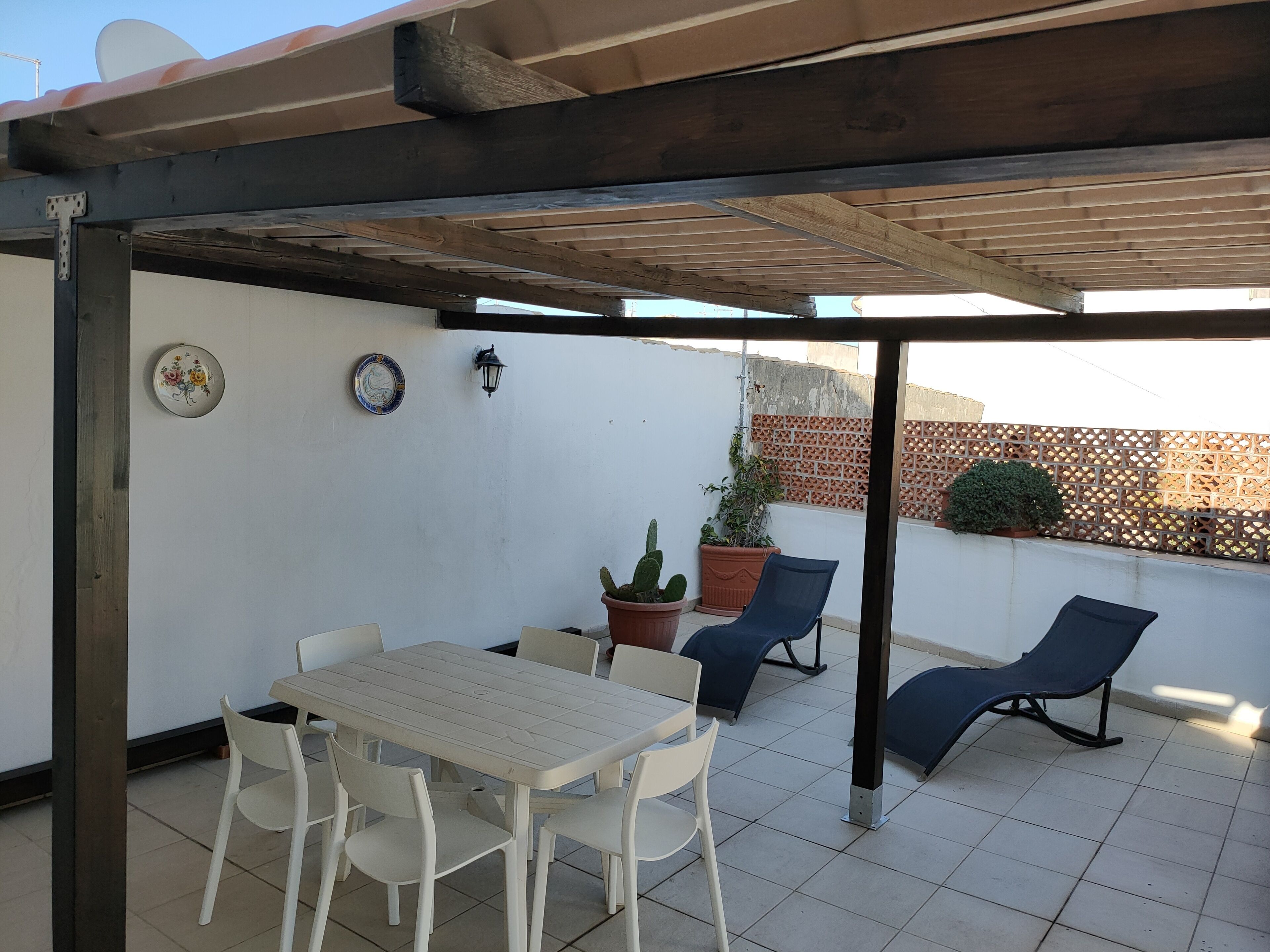 Un porche cubierto con una mesa, sillas, plantas en macetas y una silla reclinable azul.