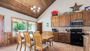 Une cuisine avec des meubles de rangement en bois, une table à manger avec des chaises, un lustre et une décoration en forme d’étoile sur le mur.