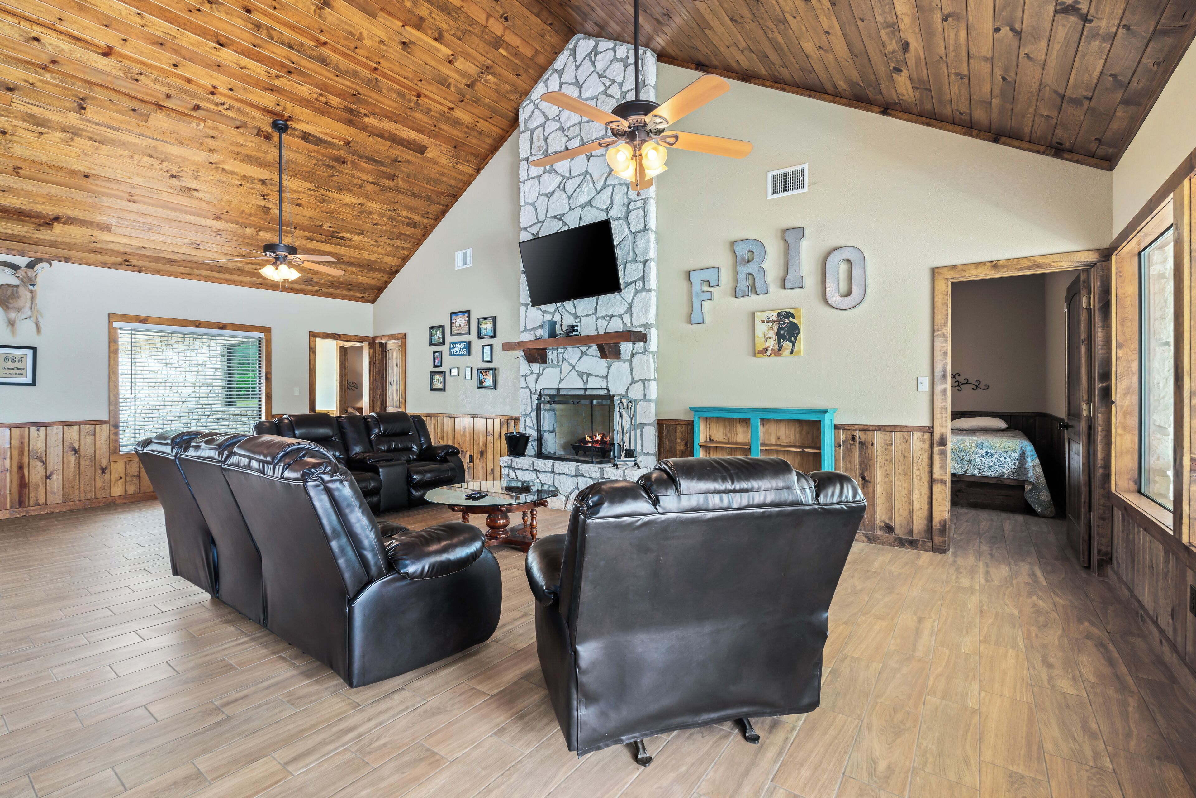 A spacious living room with leather sofas, a stone fireplace, a mounted TV, and wooden flooring.