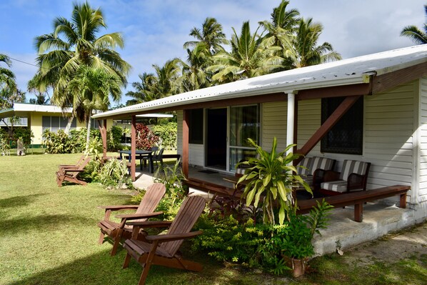 Ein Haus mit Veranda, Sitzgelegenheit im Freien und einem Rasen mit Palmen.