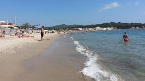Une plage où des gens se prélassent au soleil et se baignent, un ciel dégagé et des bâtiments en arrière-plan.