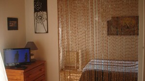 Une chambre à coucher avec un lit, un téléviseur posé sur une commode et un rideau en bambou.