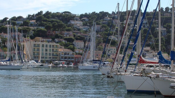 Un port de plaisance où sont amarrés de nombreux voiliers, entouré d’une ville construite sur une colline.