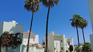 A white building with a flat roof and a small tower, surrounded by palm trees and a well-maintained lawn. - Beachfront apartment with amazing views & newly renovated with WiFi and int. TVs (Mijas)