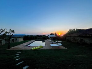 Piscina com espreguiçadeiras e um guarda-sol, cercada por um gramado e um muro de pedra.