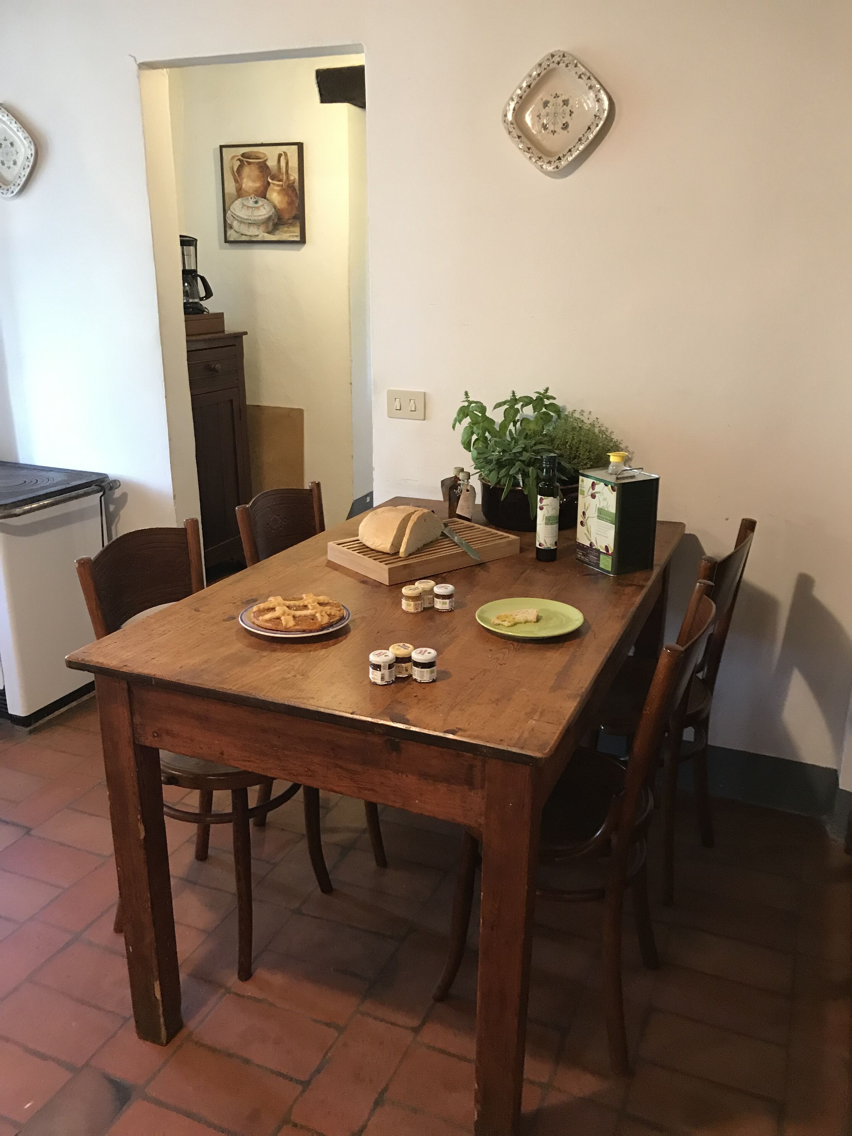 A dining table with a loaf of bread, a plate of waffles, and condiments. There is a potted plant and a bottle of wine on the table.
