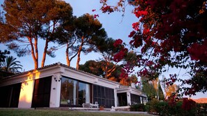 Een modern huis met grote glasramen, een terras met buitenmeubels en een verzorgd gazon.
