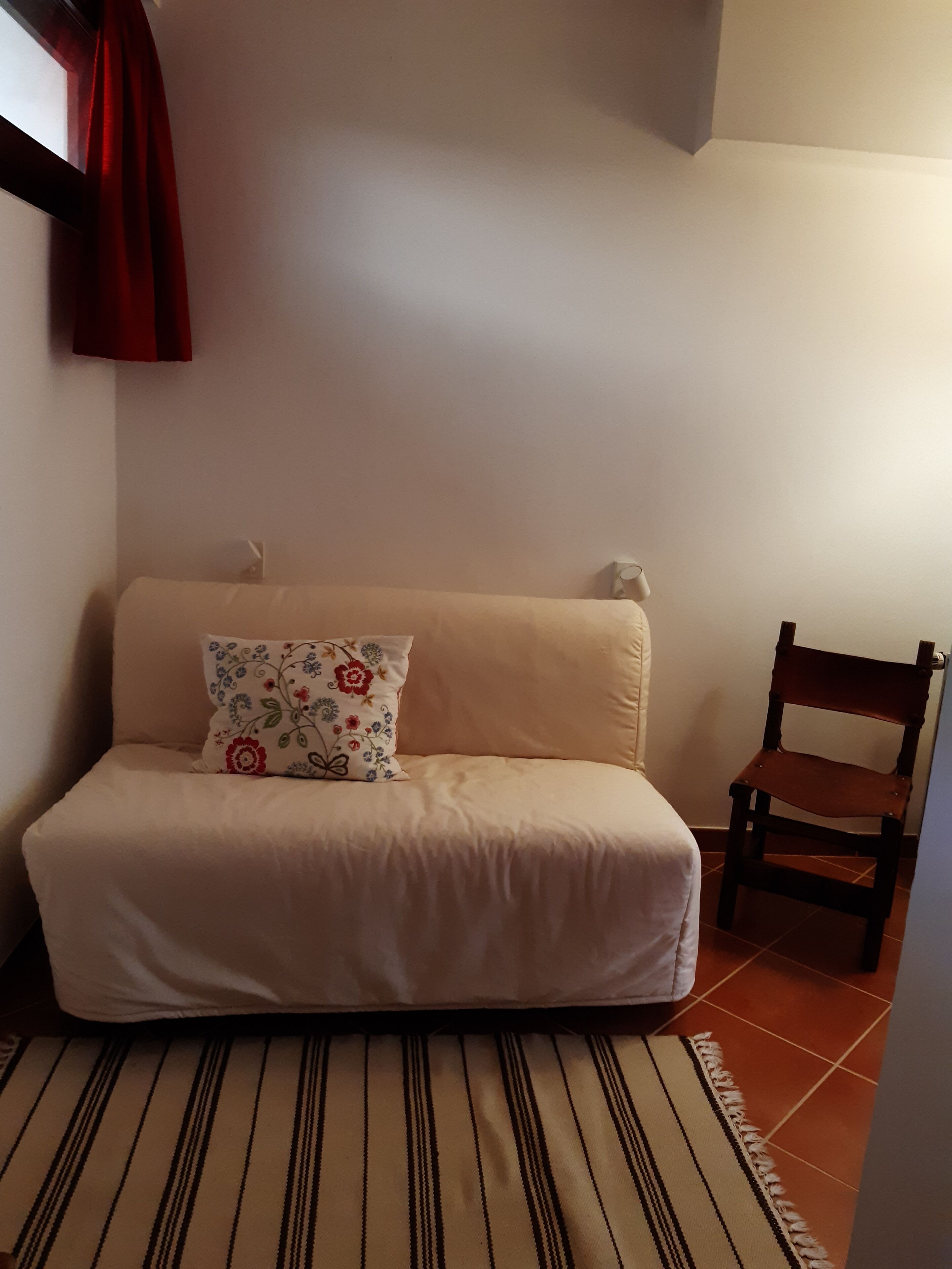 Une petite pièce accueillante, avec un canapé beige, un coussin à motifs, une chaise en bois et un tapis rayé.
