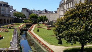 A historic courtyard with a water channel, manicured gardens, and stone buildings.