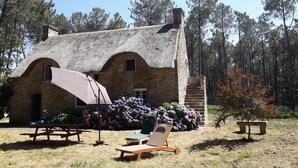 A stone house with a thatched roof, a wooden bench, and a lounge chair in front.