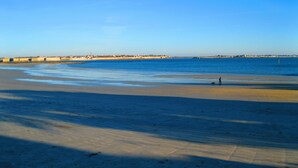 A beach with a clear sky, a sandy shore, and a distant view of buildings.