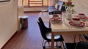 Un coin repas avec une table dressée pour quatre personnes, un canapé et une grande fenêtre donnant sur un paysage montagneux.