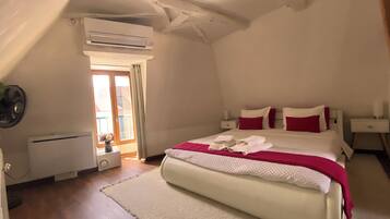 A bedroom with a bed, a bedside table, a nightstand, an air conditioning unit, a window with a view, and a door.