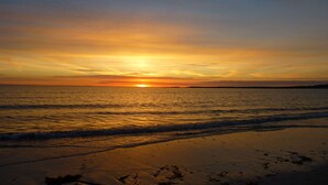 Ein Strand bei Sonnenuntergang, die Sonne geht am Horizont unter.