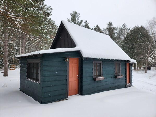 A small cabin with a steeply pitched roof, surrounded by snow-covered trees. - 2 Bedroom / 2 bath Cabin - Moreno's Cottages Celebrating 100 years! (Ray Brook)